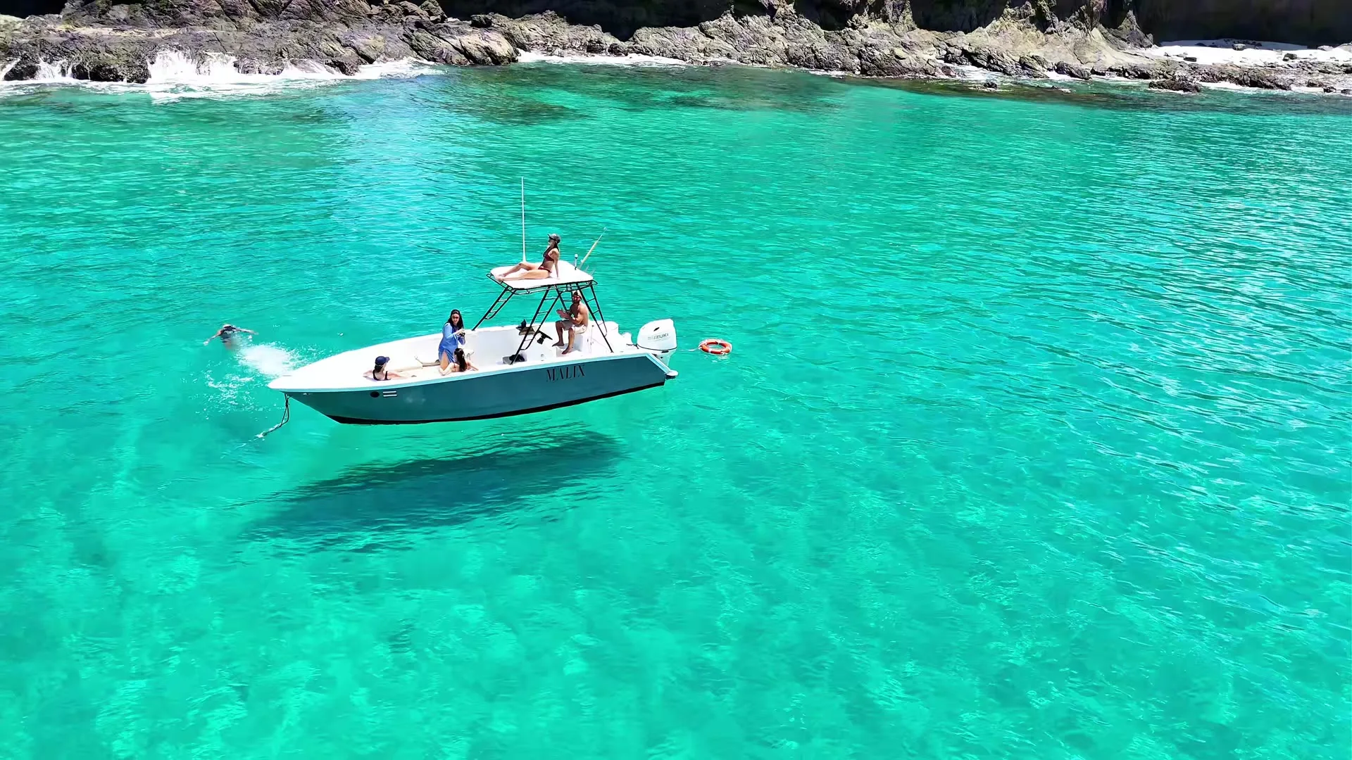 The Malix boat anchored in a hidden turquoise cove, a guest jumping into the clear water
